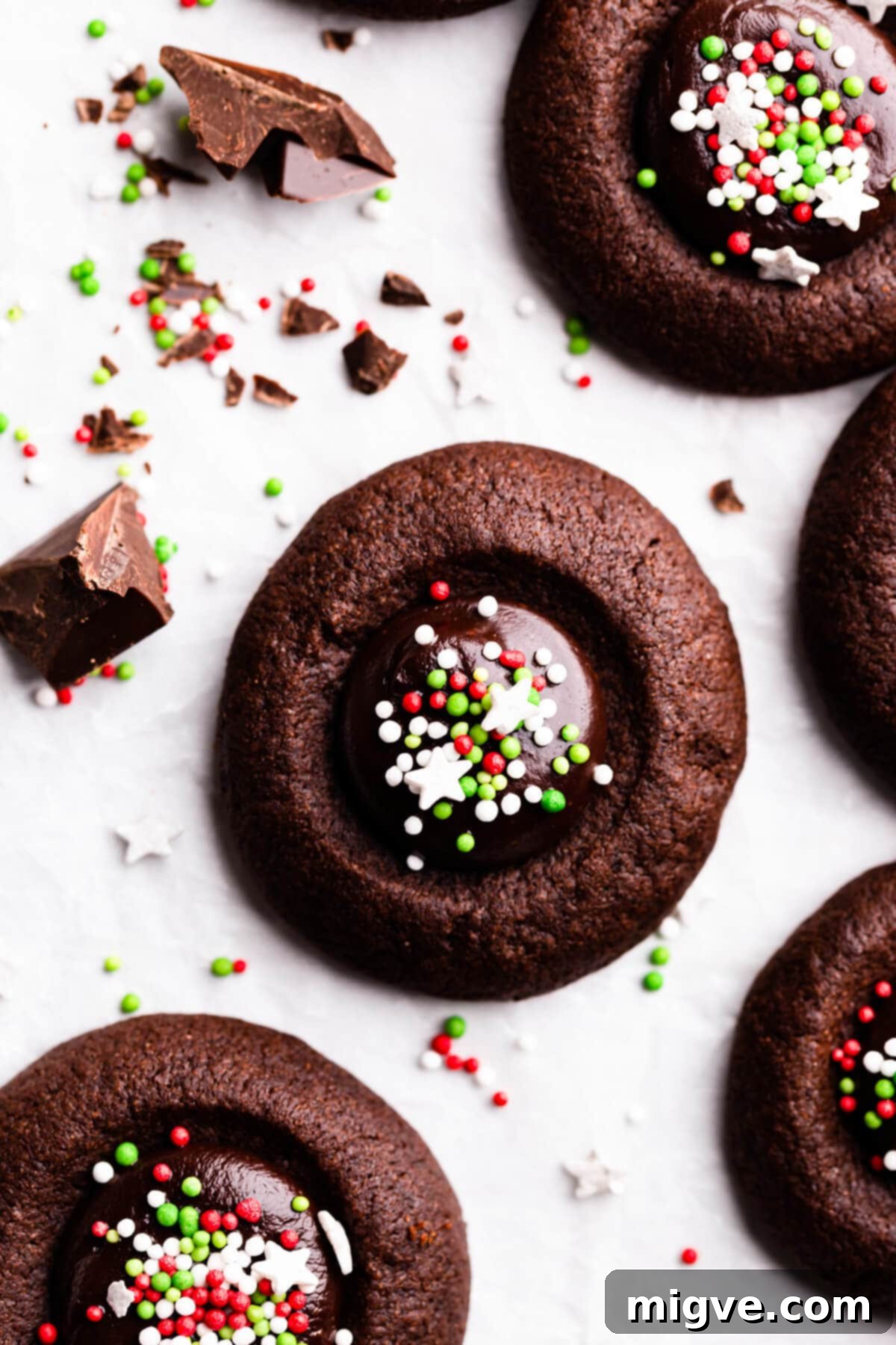 Extreme overhead close-up of a single chocolate thumbprint cookie, beautifully filled with glossy ganache and topped with a sprinkle of colorful festive decorations.