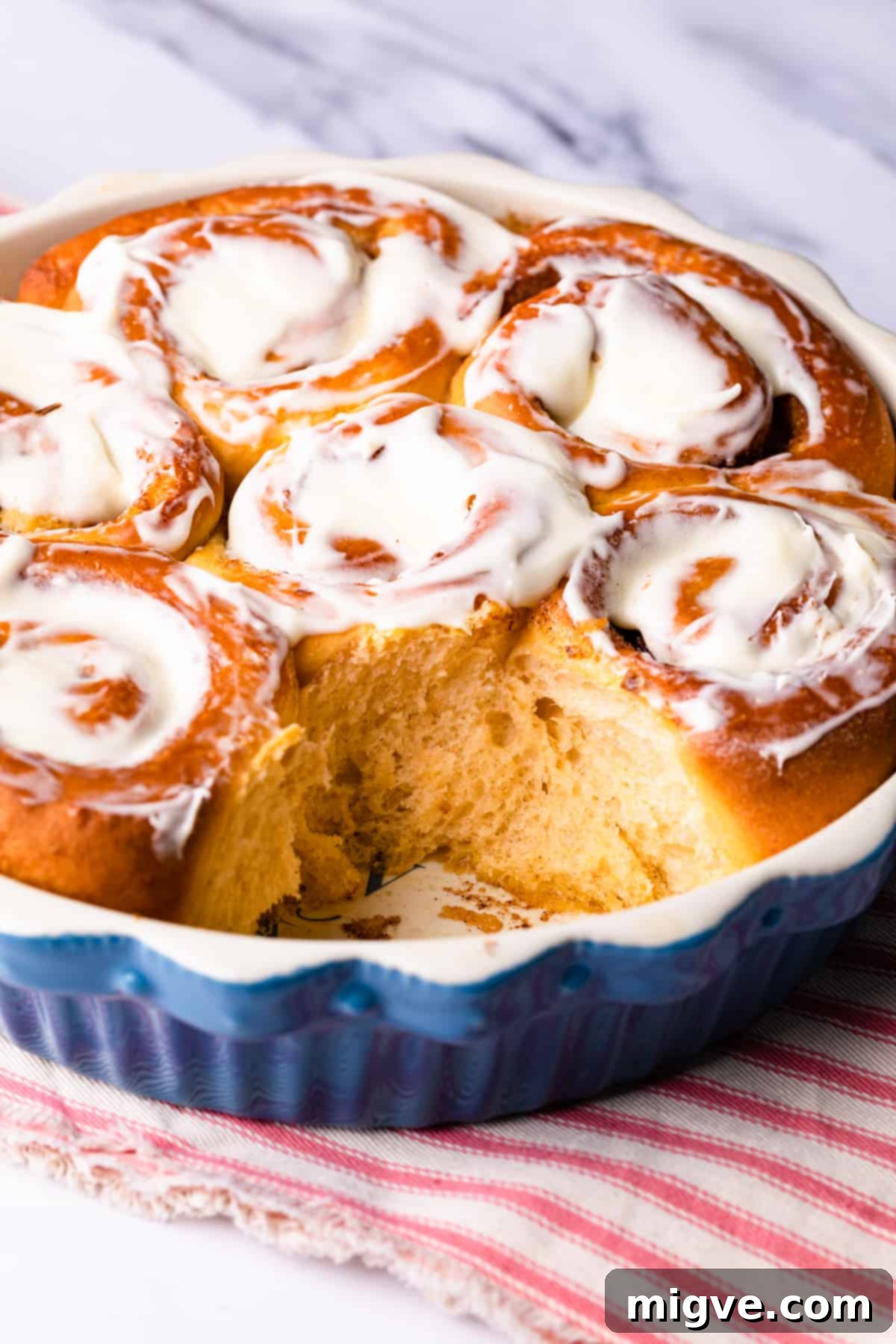 blue round pie dish with fluffy vegan sweet potato cinnamon rolls topped with frosting.