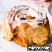 one individual vegan sweet potato cinnamon roll with bite missing and with cream cheese glaze on top.