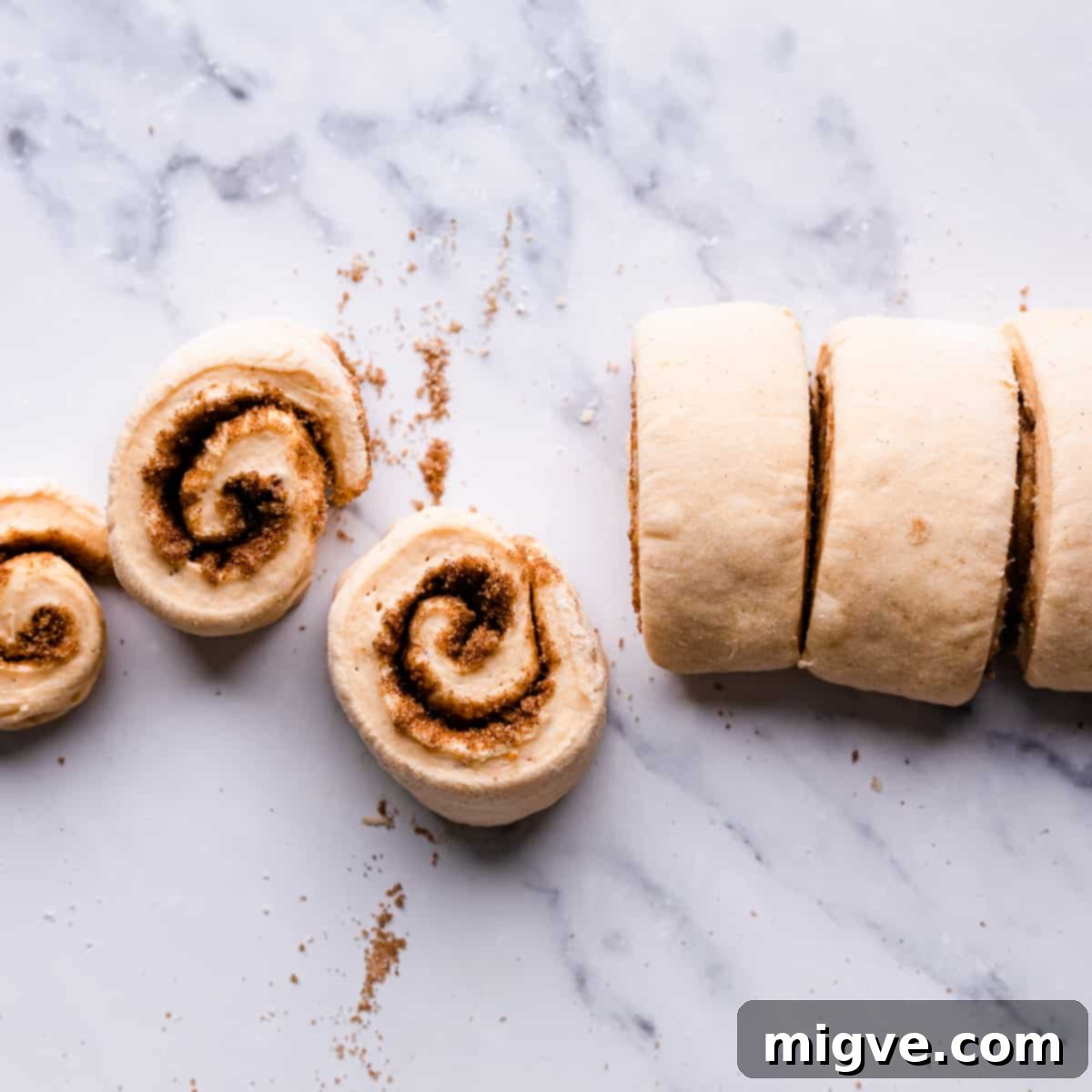 slices of dough rolls with cinnamon sugar filling on a white marble surface.