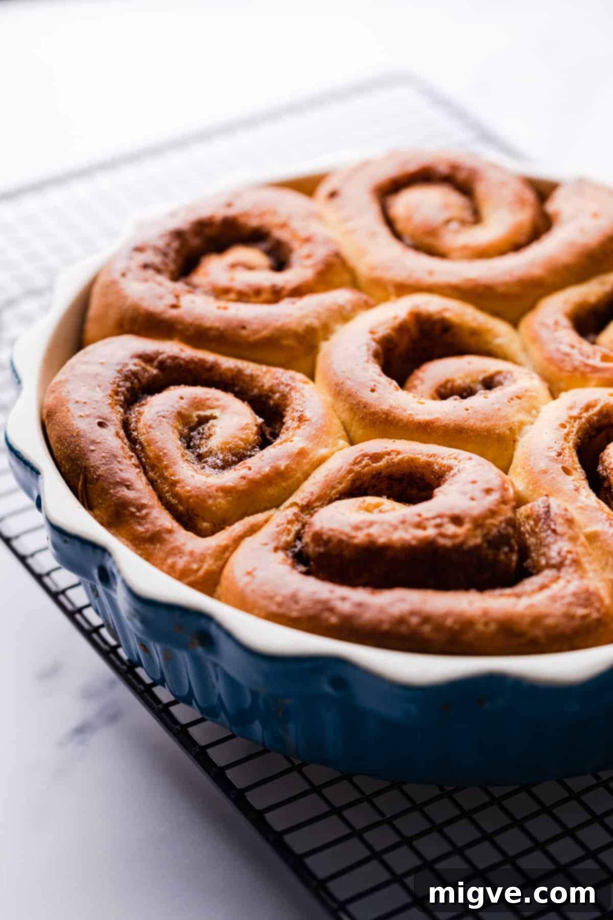 blue pie dish on a wire rack with baked sweet potato cinnamon rolls tucked inside of it.