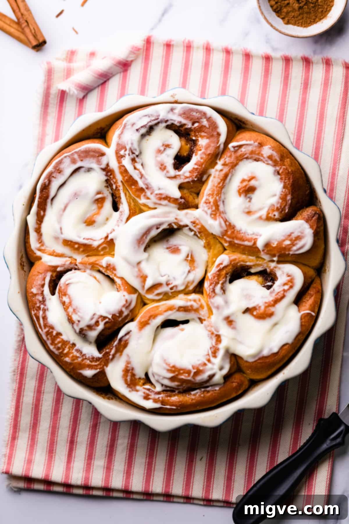 round baking dish with vegan sweet potato cinnamon buns and frosting spread on top of them.