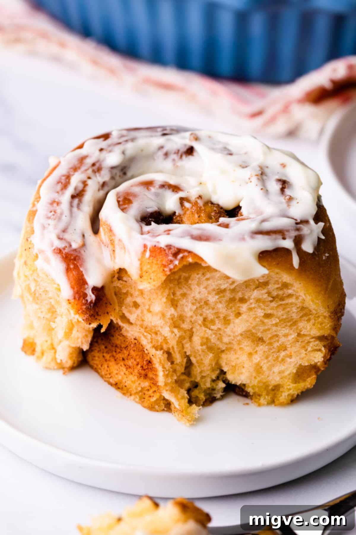 one individual vegan sweet potato cinnamon roll with bite missing and with cream cheese glaze on top.