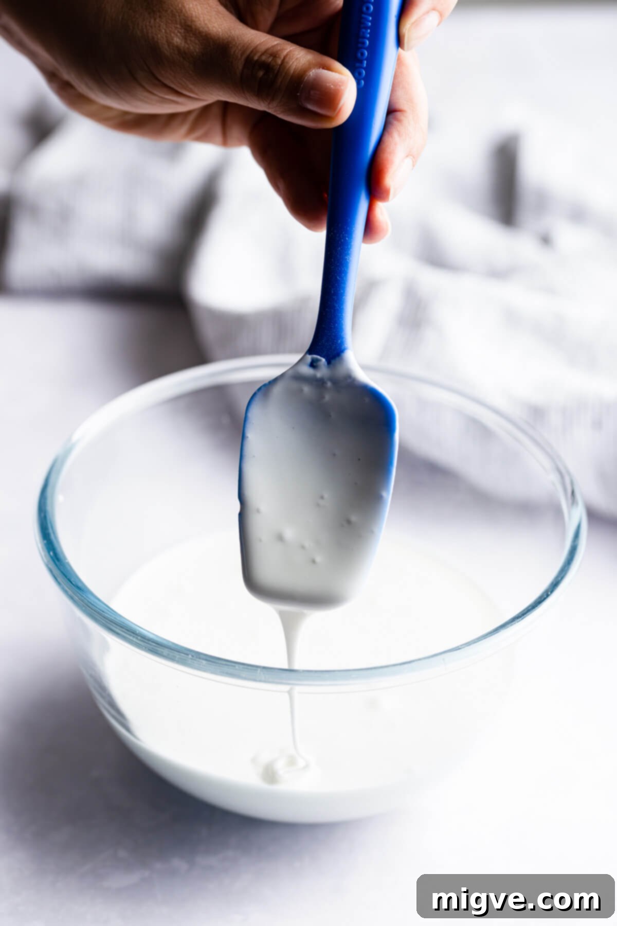 Pillowy Soft Gingerbread Cookies 9 Close-up side view of a spoon resting in a bowl filled with smooth, white royal icing, ready for decorating.