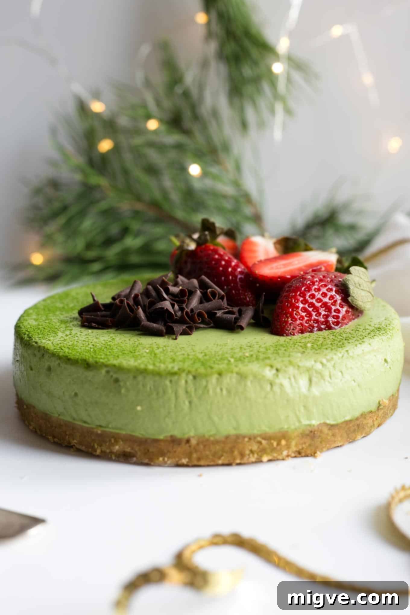 Side view of a dairy-free matcha ginger cheesecake, showcasing the distinct layers of the spiced crust and the velvety matcha filling, topped with fresh fruit.