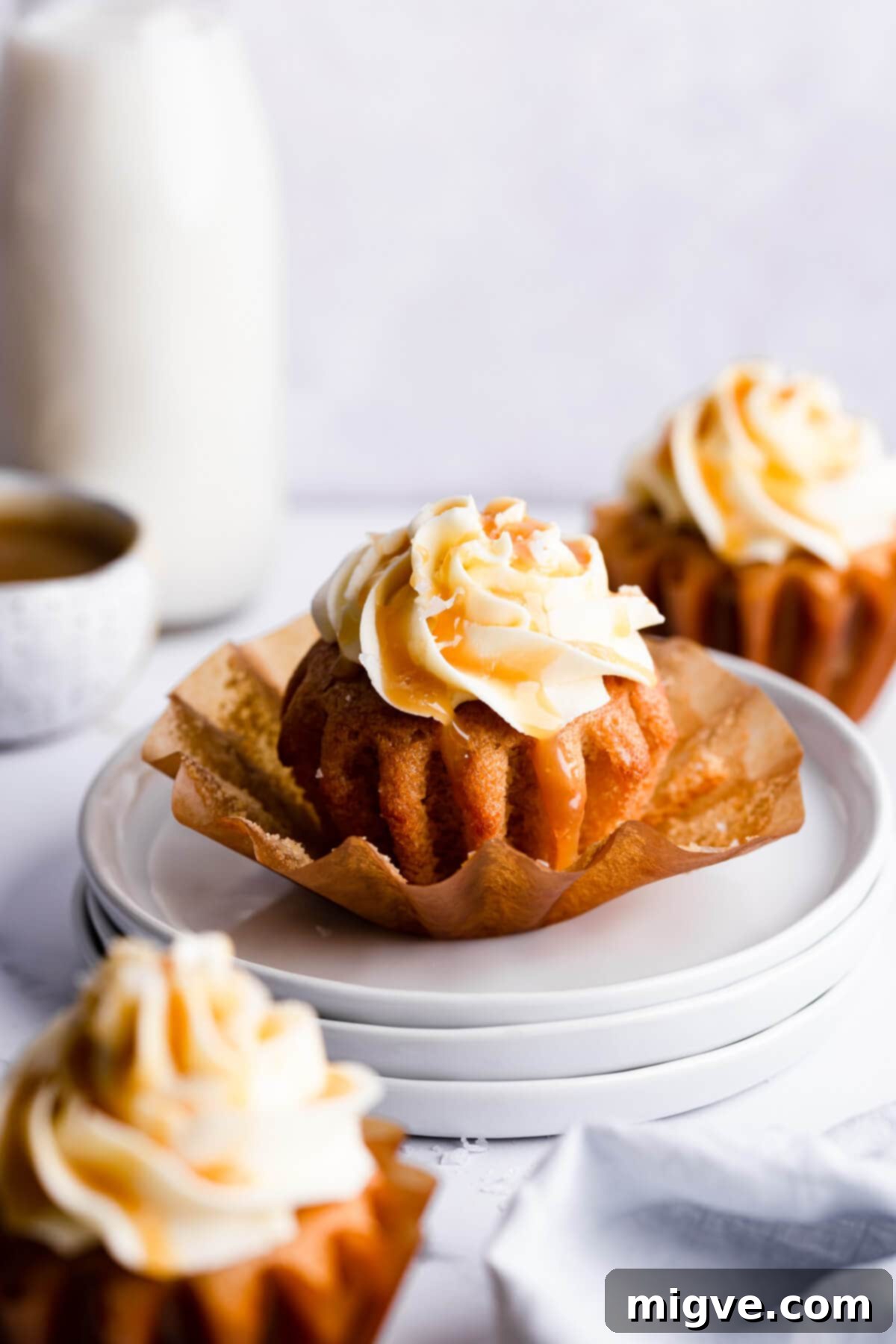 A single vegan salted caramel cupcake, out of its paper case, resting on a stack of white plates, showcasing its moist texture and caramel drizzle.