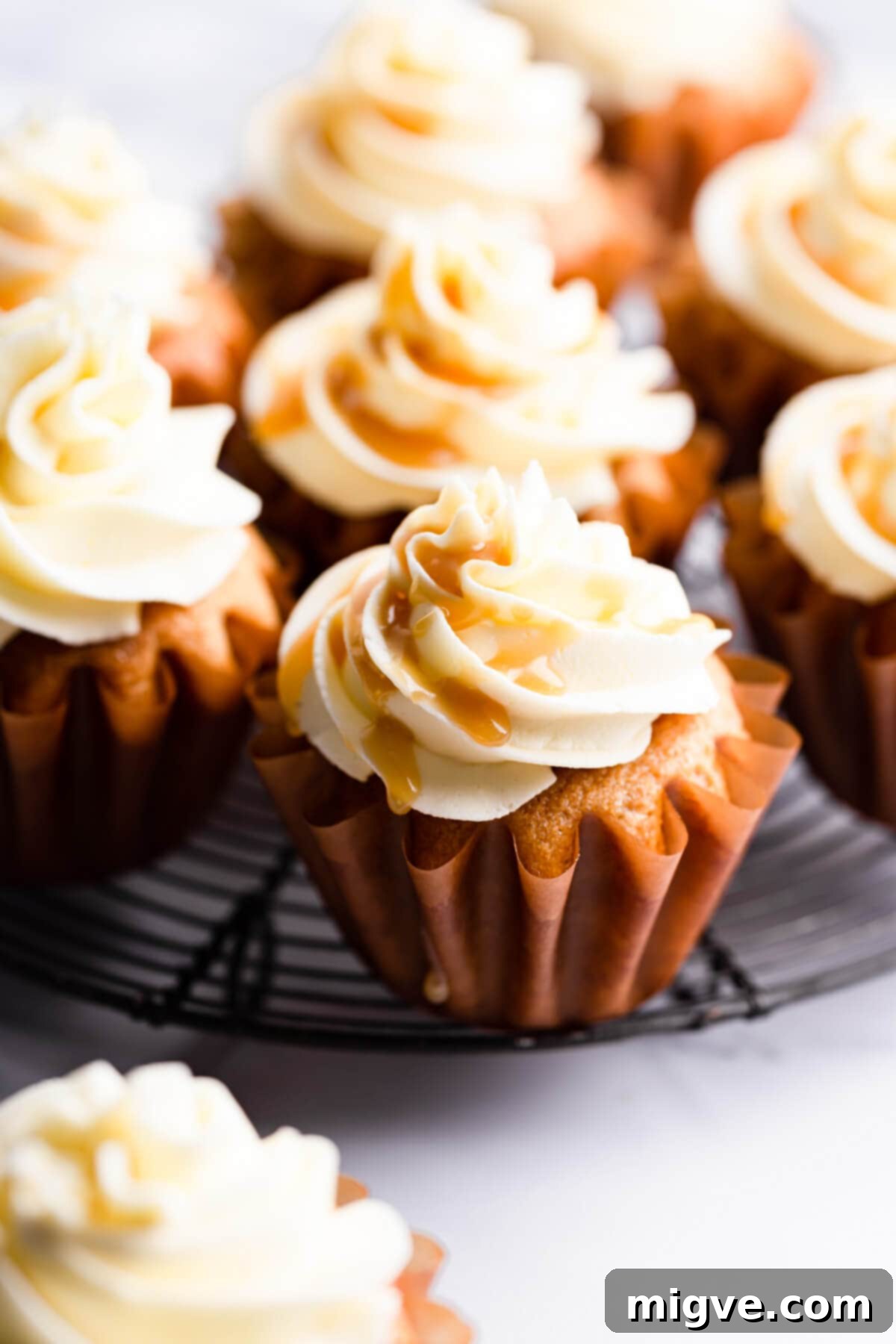 A vegan salted caramel cupcake resting on a round metal wire rack, perfectly cooled and ready for frosting.