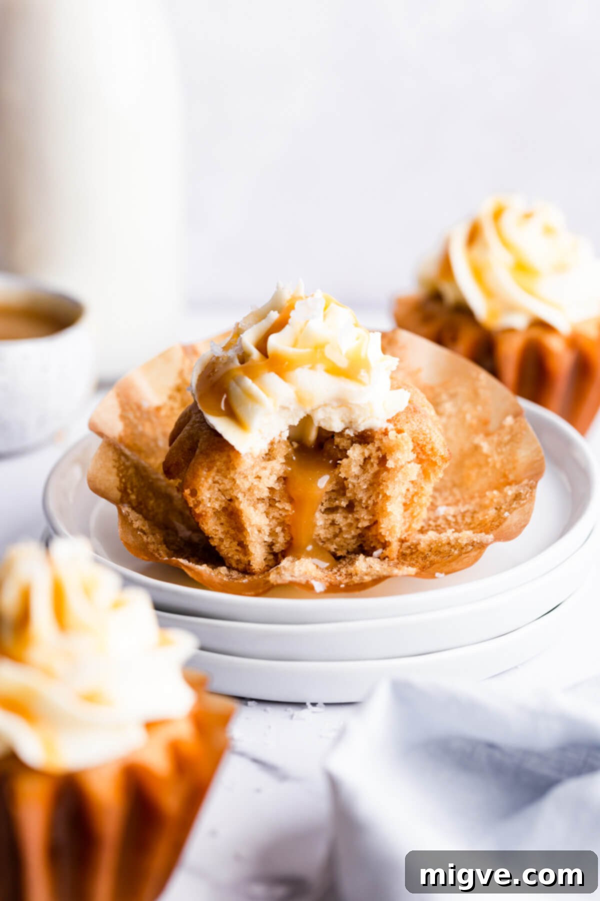 A vegan salted caramel cupcake with a bite taken out, sitting on a stack of plates, showcasing its moist texture and delicious filling.